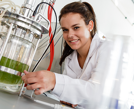 Studentin in Labor mit Glasbehälter und grüner Flüssigkeit